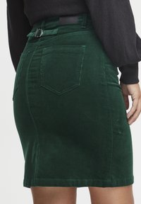Zelena korduroy suknja s prilagođenim oblikom, koja sadrži stražnji džep, vidljive šavove i detalj s remenom u tonu na struku.