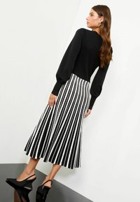 Melnā ribotā garo pieduru blūze, savienota ar melnbaltu svītrainu plisētu midi svārku. Modelis valkā melnas slingback augstādas.