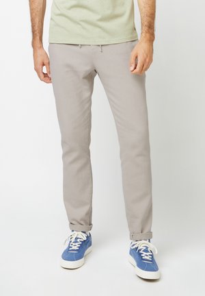 Lichtgrijze chino broek met een slim fit, voorzien van een koord in de taille, opgerolde manchetten en een zachte textuur. G gedragen met blauwe sneakers.