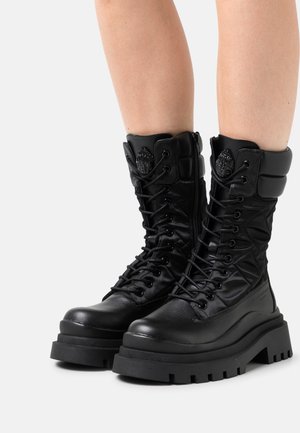 Sorte snørebånds-støvler med en robust sål, der kombinerer læder og polstret nylon, med et præget logo på skaftet.