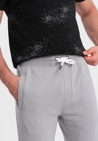 Graue Sweatpants mit elastischem Bund, weißem Kordelzug und zwei seitlichen Taschen. Das Material wirkt weich und bequem.