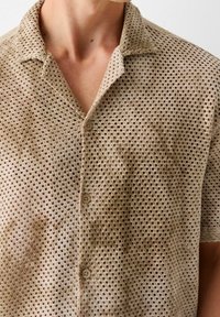Lichtbruin shirt met korte mouwen van meshstof met een kraag met knopen. Voorzien van ronde gaten voor ademend vermogen.