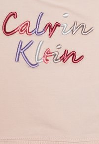 Tejido de color rosa claro con bordado del texto "Calvin Klein" en varios colores: rojo, púrpura y blanco, que presenta una textura suave y una costura prolija.