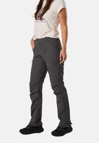 Woman wearing black outdoor pants with multiple zippered pockets, black hiking shoes, and a beige graphic t-shirt.