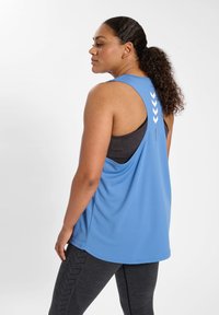 Blue athletic tank top with a loose fit, featuring back cutout, white chevron accents, and paired with textured dark gray leggings.