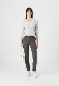 Gray sweater with a v-neck, paired with gray skinny jeans. Lightweight texture, white sneakers, and a small white handbag.