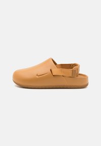 Nike slip-on sko i tan, laget av glatt gummi med teksturert såle, med en sidestropp for sikker passform og rund tådesign.