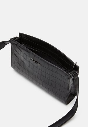 Czarna prostokątna torebka z tłoczonym wzorem krokodyla, srebrnym zamkiem i cienkim paskiem na ramię, widziana z góry pod kątem.