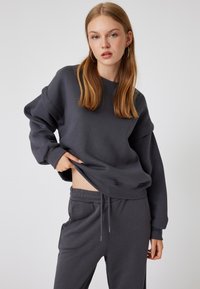 Sudadera de gran tamaño color gris oscuro, con puños y dobladillo acanalados, combinada con pantalones de tiro ajustable a juego, que presentan una textura suave.