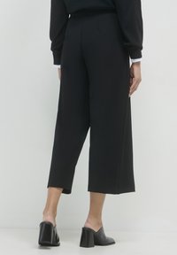 Pantaloni neri a gamba larga realizzati in tessuto liscio, con vita alta e tasche laterali. Abbinati a mule nere con tacco, che offrono una silhouette strutturata.