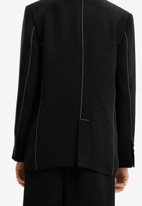 Czarna marynarka z białym kontrastowym przeszyciem. Posiada usztywnione ramiona, mankiety na guziki oraz pojedyncze rozcięcie z tyłu.