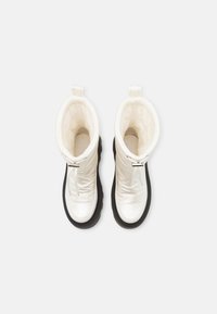 Białe ocieplane buty z błyszczącym wykończeniem, czarną gumową podeszwą i tekstylnym wnętrzem. Posiadają uchwyt do chwytania i zamek błyskawiczny.