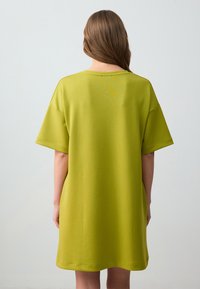 Abito t-shirt oversize verde lime con maniche corte, realizzato in tessuto morbido, presenta un collo a giro modesto e arriva sopra il ginocchio.