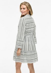 Robe blanche avec des motifs géométriques noirs, manches longues et silhouette évasée. Présente une taille cintrée et un tissu texturé.
