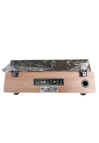 Dispositivo de audio de madera con una parte superior negra brillante, que presenta un panel de control con puertos y un orificio para el altavoz redondo en un lado. Está parcialmente cubierto con envoltorio de plástico.