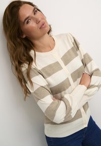 Lightweight striped cardigan in cream and beige, featuring a button-down front, ribbed cuffs, and soft texture. Worn with dark jeans.