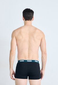 Schwarze Boxershorts mit einem grünen und weißen logowierten Bund, aus Baumwollmaterial gefertigt und im taillierten Design, von der Rückansicht.