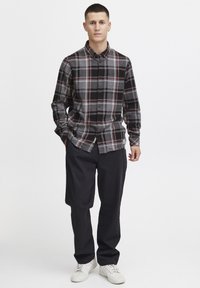 Schwarz-grau-rote karierte Hemd mit Button-down-Kragen, langen Ärmeln und gerafften Manschetten, kombiniert mit schwarzen Hosen und weißen Turnschuhen.