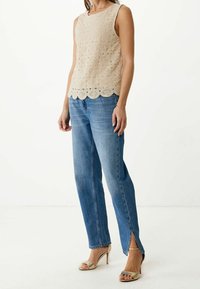 Haut beige sans manches avec motif crochet et ourlet festonné, associé à un jean droit bleu clair et des sandales à talons dorés.