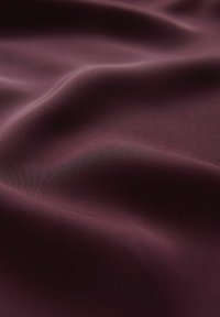 Bordeaux satin stof med en glat tekstur, der viser subtile folder og en glans, der fremhæver dens flydende natur. Ideel til drapering eller polstring.