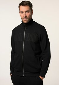 Sudadera negra con cremallera hecha de tela suave, con un alto cuello y la palabra "IRON" en letras en relieve en el pecho.