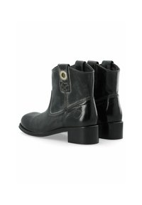 Botas de cuero negro hasta el tobillo con puntera redondeada, tacón cuadrado y paneles elásticos dobles en los laterales. Incluyen un botón decorativo en el lado exterior.