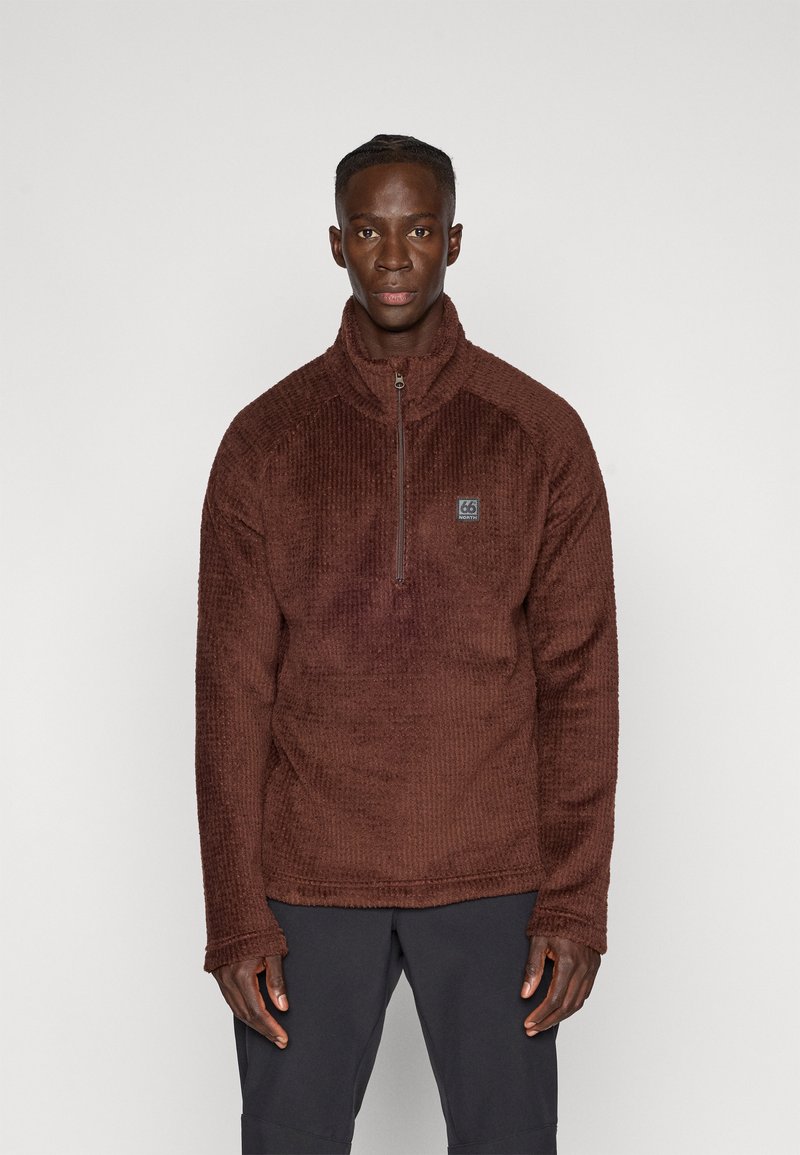 Brauner Fleece-Pullover mit einem Viertel-Reißverschluss, strukturierter Oberfläche, hohem Kragen und einem kleinen Logo-Patch auf der Brust. Lange Ärmel, lockere Passform.