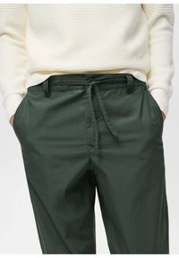 Dark green trousers with a drawstring waistband, button closure, and side pockets. Smooth fabric and notched front design.