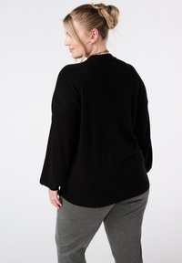 Zwarte gebreide trui met een losse pasvorm, verlaagde schouders en lange mouwen. Gecombineerd met grijze broek, met een gladde textuur en minimalistisch ontwerp.