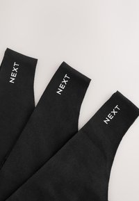 Trois bracelets en tissu noir avec le mot NEXT imprimé en blanc sur chacun, disposés côte à côte sur une surface claire.