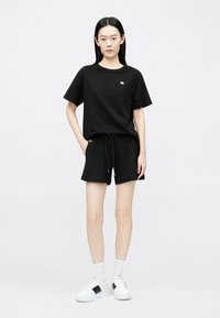 Čierne bavlnené tričko s krátkymi rukávmi, spárované s čiernymi šortkami s šnúrkou. Nosí sa s bielymi teniskami a ponožkami.