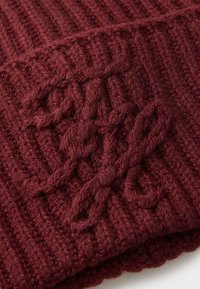 Gros plan sur un tissu en tricot rouge foncé présentant un motif en maille torsadée avec des points tressés et torsadés.