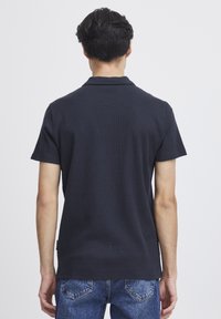Marineblå polo skjorte med korte ermer og teksturert stoff, med klassisk krage og rett snitt, kombinert med lyseblå jeans.