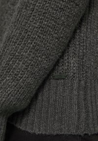 Ciemnoszary sweter wykonany na drutach z teksturowanym wzorem, prążkowanym dołem oraz małą czarną metką z napisem "QS" z boku.