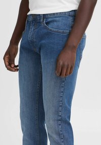 Jeans de mezclilla azul con corte ajustado, que cuentan con bolsillos estándar, cierre de botones y un ligero desgastado para un aspecto texturizado.