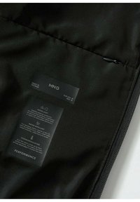 Black puffer jacket interior showing care label. Features includes water-repellent material, smooth texture, and zipper detailing.