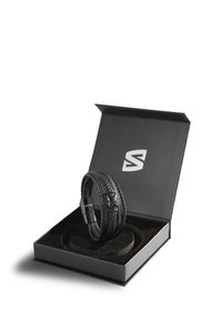 Black leather bracelet with woven texture, showcased in a black box with a cushioned interior. Box features a logo on the lid.