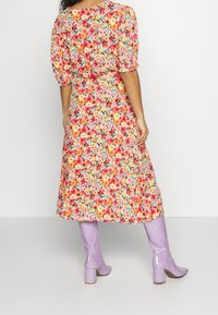 Abito midi floreale con maniche a sbuffo in un motivo colorato su sfondo chiaro; abbinato a stivali al ginocchio lucidi e di un delicato colore lavanda.