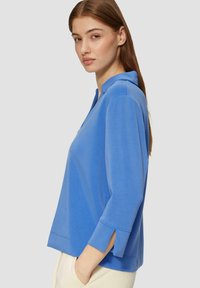 Pull bleu à col, manches trois-quarts et fentes sur les côtés. Texture lisse et coupe décontractée. Présente un minimum de détails de couture.