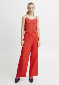 Camisón rojo con encaje, combinado con pantalones rojos de pierna ancha. El modelo lleva tacones negros y calcetines magenta, contra un fondo blanco.
