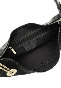 Interno di una borsa a tracolla in pelle nera, con una tasca con cerniera, foderatura in tessuto morbido e un accento in catena dorata con un dettaglio hardware rotondo.