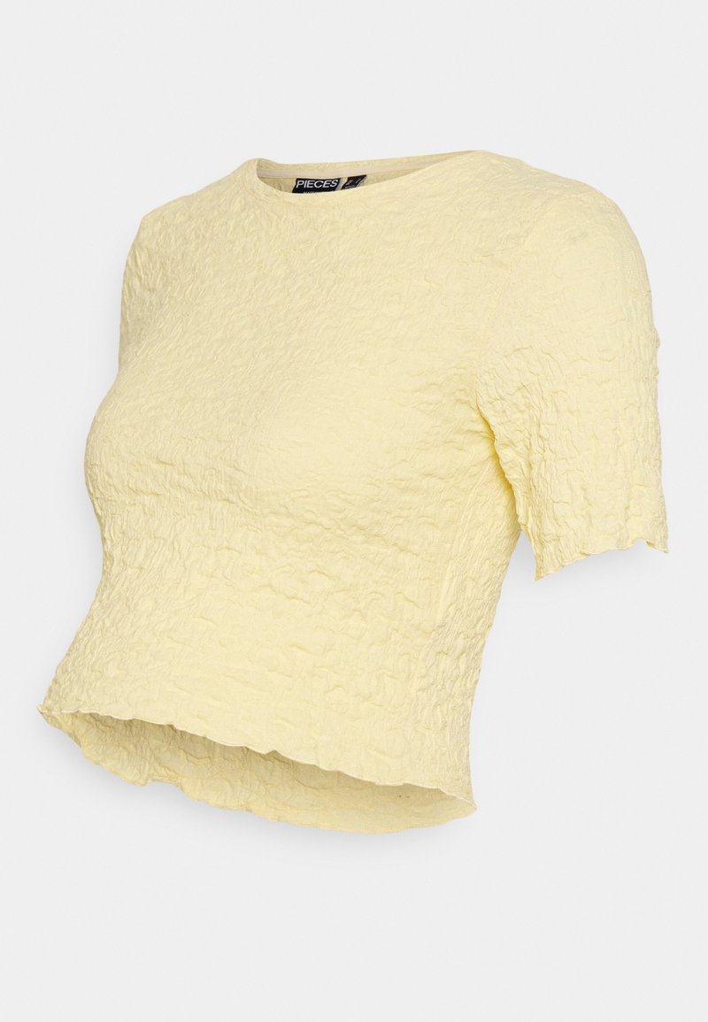 Haut jaune à manches courtes avec une surface texturée et froissée. Encolure ronde et ourlet légèrement court avec une finition brute. Étiquette de marque visible.