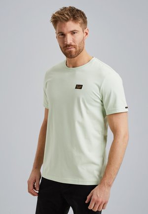 T-shirt vert clair à manches courtes en coton, avec un col rond et une petite étiquette noire sur la poitrine. Texture lisse.
