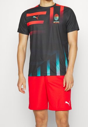 Maglia sportiva nera con strisce rosse e teal, con il logo Puma e il crest dell'AC Milan. Abbinata a pantaloni corti rossi brillanti.