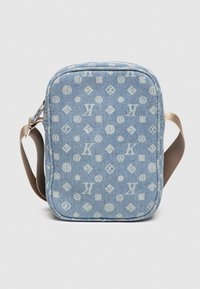 Modrá denimová crossbody taška s opakujúcim sa svetlým logom, zipsovým uzáverom a hnedým nastaviteľným popruhom. Obdĺžnikový tvar.