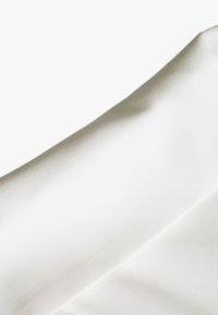 Tissu blanc texturé avec un drapé lisse et diagonal. Le matériau semble léger avec un subtil éclat, offrant un look épuré et minimaliste.