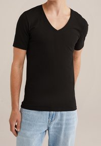 Maglietta a maniche corte in cotone nera con scollatura a V, design aderente, texture liscia e uno stile pulito e minimalista. Indossata con jeans azzurri chiari.