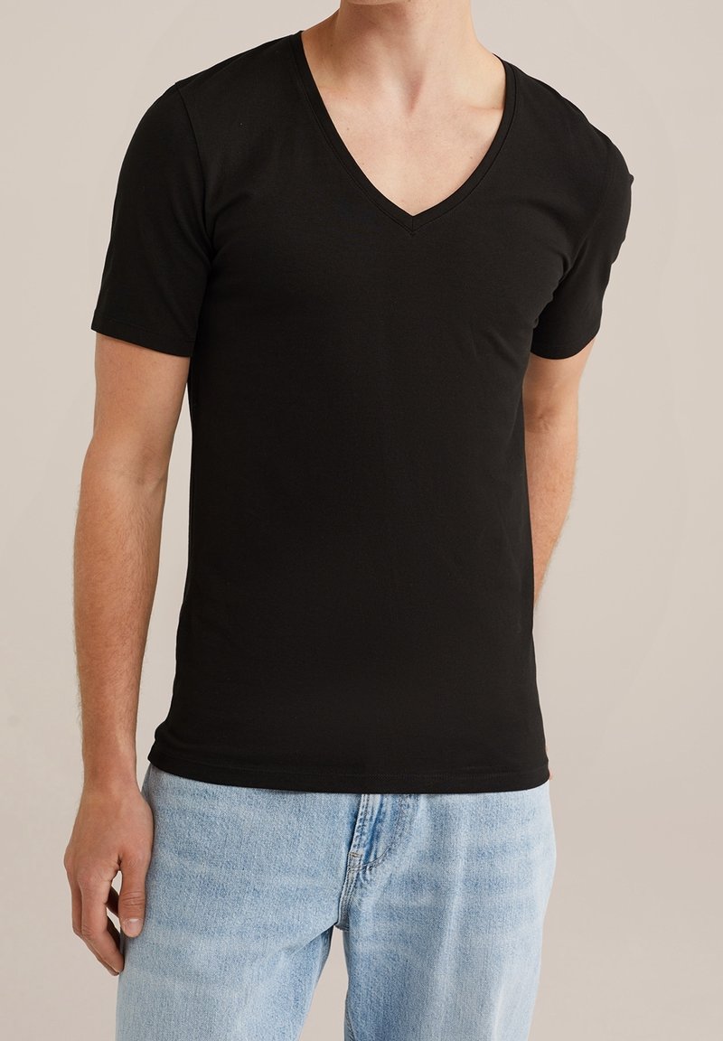 Maglietta a maniche corte in cotone nera con scollatura a V, design aderente, texture liscia e uno stile pulito e minimalista. Indossata con jeans azzurri chiari.