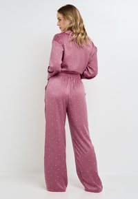Ensemble de loungewear rose avec un haut à col et un pantalon à taille élastique, présentant un subtil motif de cœurs blancs sur un tissu doux et lisse.