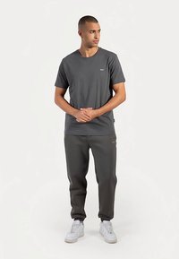 Graues Baumwoll-T-Shirt mit rundem Ausschnitt und kleinem Logo auf der Brust, kombiniert mit grauen Jogginghosen und weißen Sneakern.